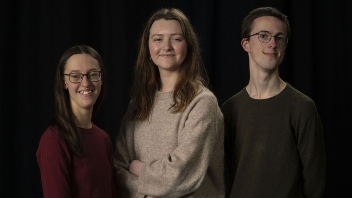 Tre personer, der står sammen og smiler.