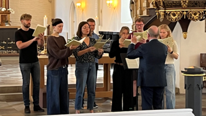 Et kor øver eller optræder med salmer i en kirke, ledet af en dirigent med noder.