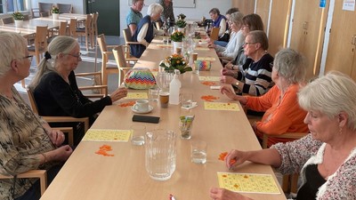En gruppe mennesker samlet omkring et langt bord og spiller et kortspil i en lys indendørs omgivelse.