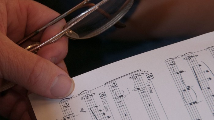 Hand hält Brille über aufgeschlagenem Buch mit Notenblatt