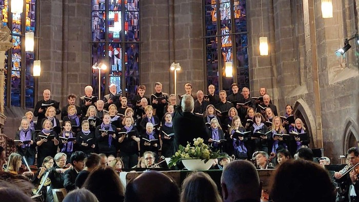 Ein Chor tritt in einer prächtigen Kathedrale mit farbenfrohen Buntglasfenstern und einer von Kerzenlicht durchfluteten Atmosphäre auf.