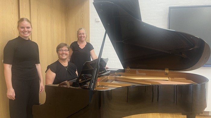 Tre kvinder ved et sort piano
