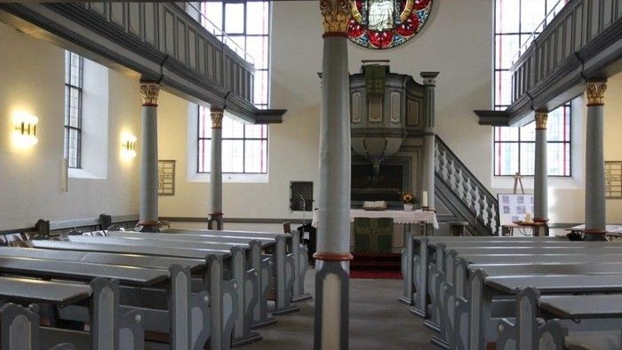 Innenraum einer Kirche mit hölzernen Bänken und einem großen Fenster.