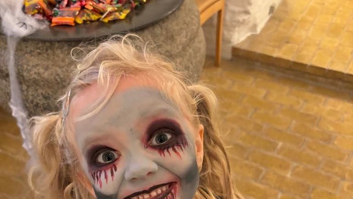 Et lille pige med horror-makeup og grå overall.