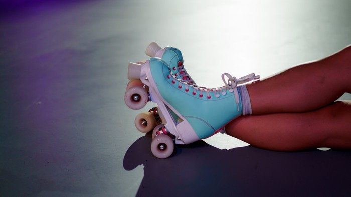 Ein Paar Rollschuhe in Blau und Rosa, getragen von einer Person auf einer Rollschuhbahn