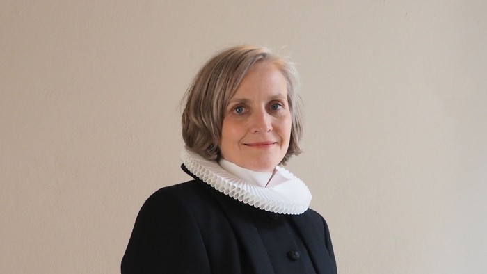 Kvinde i sort kaptajnmø, hvid krage og hvid kuffe.