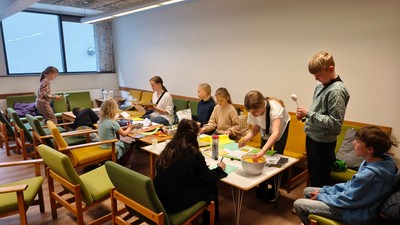 En gruppe børn sidder om bord i en lokal og laver håndarbejde.