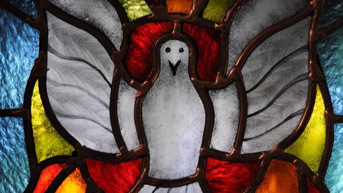 Kirchenfenster mit der Darstellung des Heiligen Geistes als weiße Taube, umgeben von einem gelben Kreis und drei Flammen