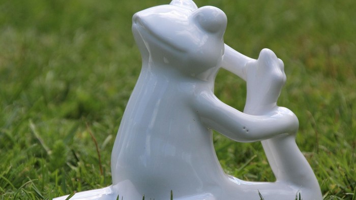 Eine verspielte weiße Keramik-Froschfigur, die eine winzige Geige auf Gras hält.