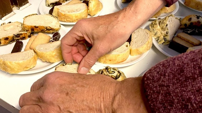 Person, die Gebäck von einem Büfett-Tisch mit verschiedenen gefüllten Gebäckstücken auf Tellern auswählt.