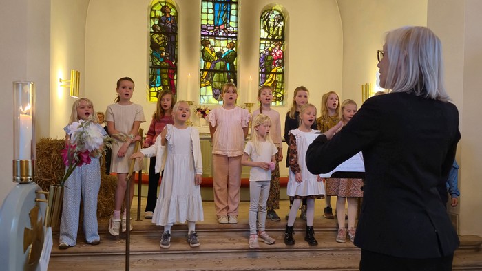 En gruppe børn og en kvinde står i en kirke.