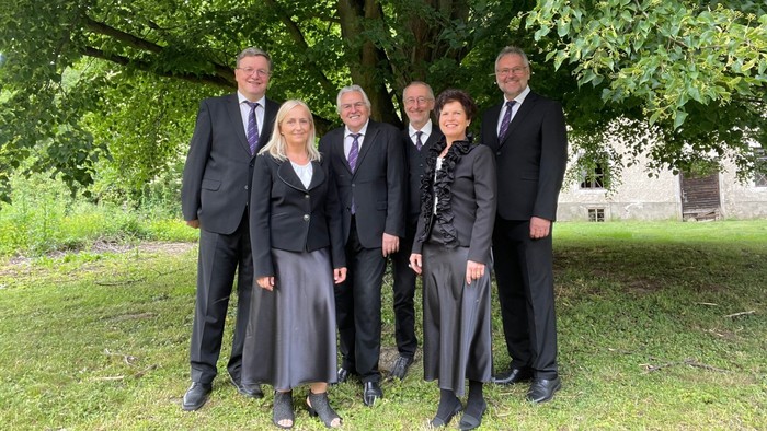 Eine Gruppe von sechs Personen posiert formell im Freien unter einem Baum