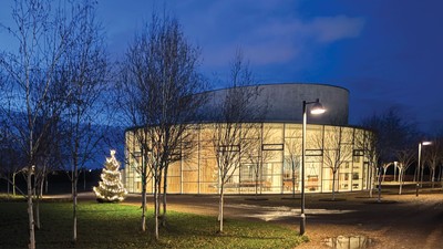 En moderne bygning med en stor rund del, belyset ved natten med et juletree foran