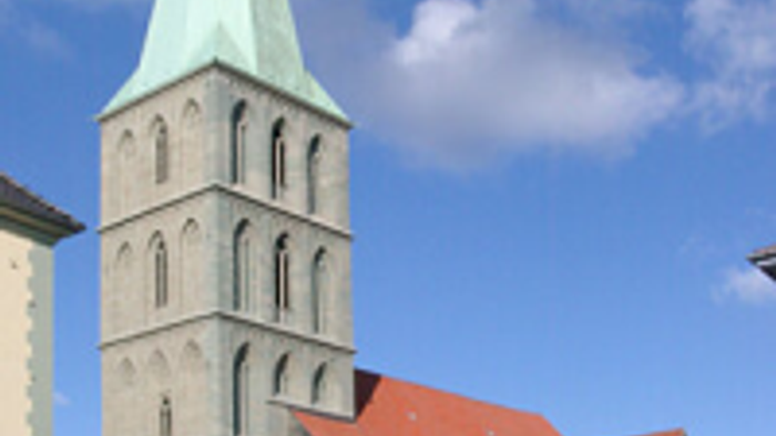 Große Kirche mit hohem Turm und rotem Dach vor blauem Himmel.