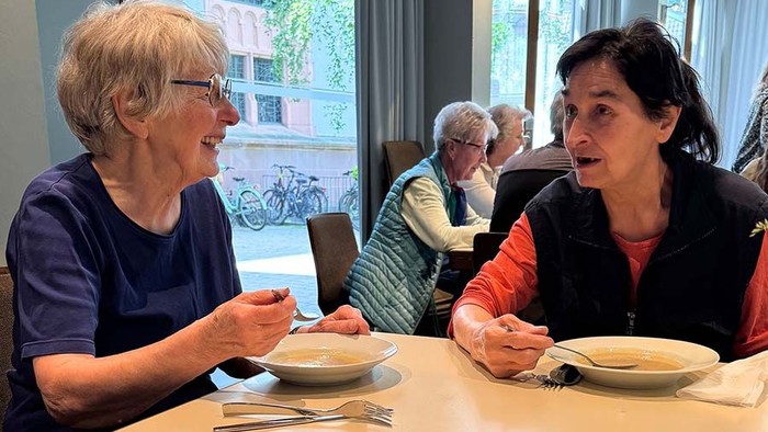 Zwei Frauen genießen gemeinsam eine Mahlzeit in einem gemütlichen Essbereich mit anderen im Hintergrund.