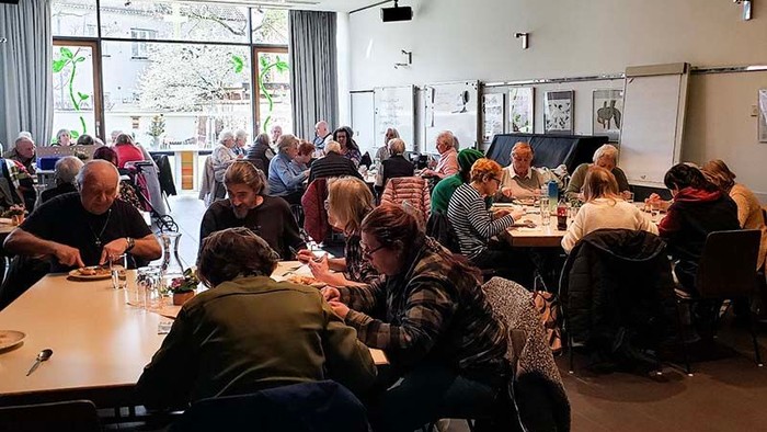 Gruppe von Menschen, die sich in einem gemütlichen Innenbereich an Tischen versammelt haben und sich bei Gesprächen und gemeinsamen Mahlzeiten unterhalten.