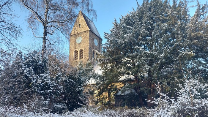 Schneebedeckte Bäume und ein Kirchturm mit Uhr im Winter