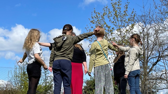 En gruppe af unge står sammen i en park og kigger op i træerne.