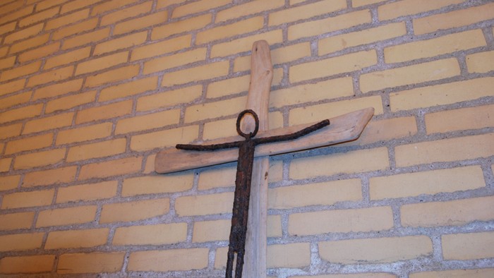 En trækorsfigur hænger på en mur af gule mursten.