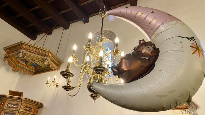 En stor blå ballong med en bjørn i den hænger fra taket under en kronesæde.