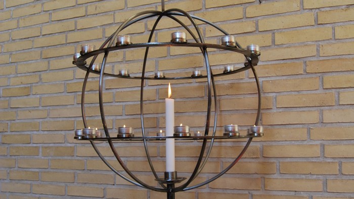 En globusformet kandleholder med flere lyse candler foran mur af gule mursten