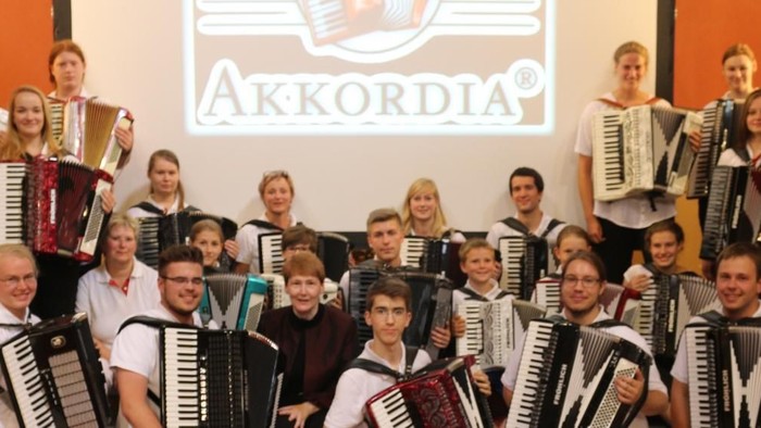 Ein großer Akkordeon-Ensemble vor einem Schild mit der Aufschrift