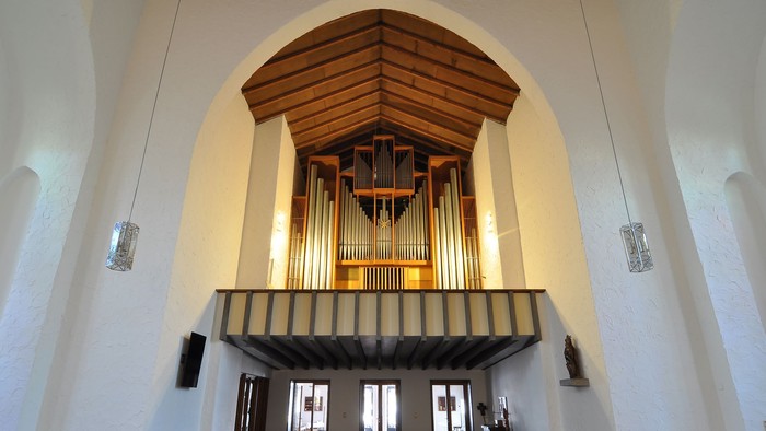 Elegante Kircheninnenausstattung mit einer großen Pfeifenorgel über hölzernen Kirchenbänken unter einem gewölbten Deckengewölbe.