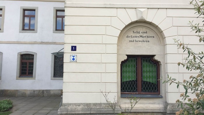 Das Bild zeigt ein weißes Gebäude mit einem kleinen Fenster und einer grünen Fensterbank.