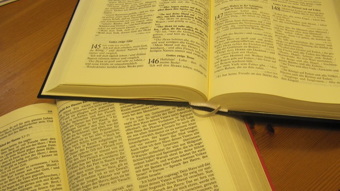 Zwei aufgeschlagene Bücher liegen auf einem Holztisch