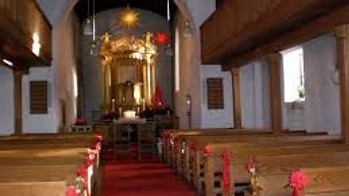 Die Kirche mit roten Teppich und Holzbänken, beleuchtet von natürlichem Licht.