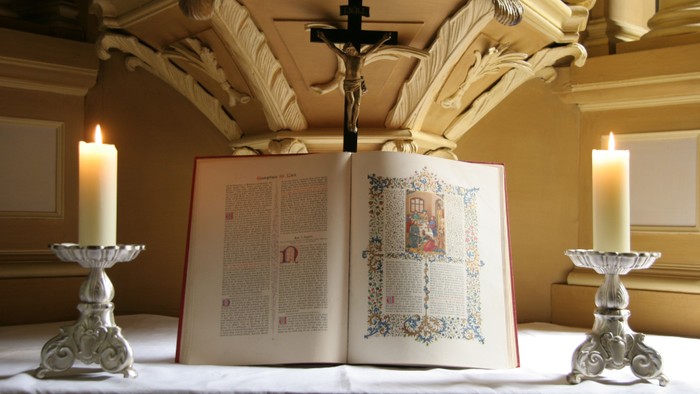 Ein offenes Buch mit Kreuz und Kerzen auf einem Altar