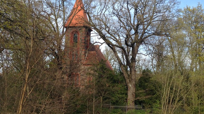 Ein kleiner roter Ziegelbau mit spitzem Dach steht in einem bewaldeten Gebiet.
