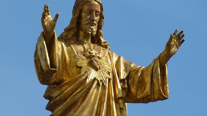 Goldene Jesus-Statue mit ausgebreiteten Armen vor blauem Himmel