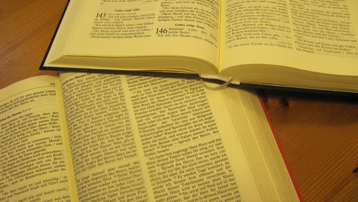 Zwei aufgeschlagene Bücher liegen auf einem Holztisch