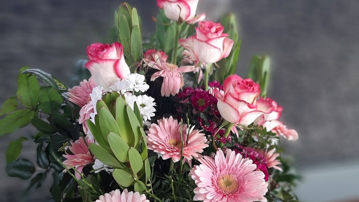 Ein Blumenstrauß mit rosa Rosen und Gerbera steht vor einem Kreuz.