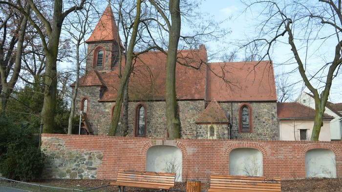 Kleine Kirche mit rotem Dach und drei Bänken davor