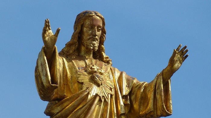 Goldene Jesus-Statue mit ausgebreiteten Armen vor blauem Himmel