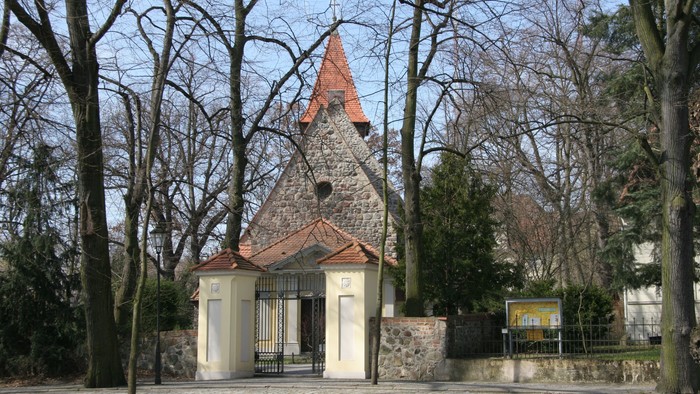 Kleines weißes Gebäude mit spitzem Dach und rotem Dach in parkähnlichem Gebiet