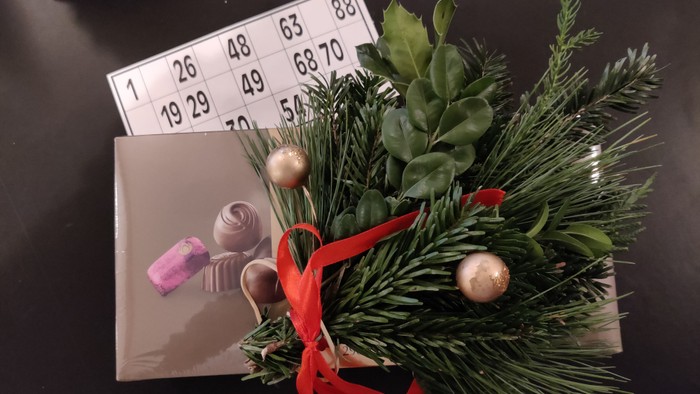 En lille juledekorationsstykke med grønne nåler, røde bånd og guldglokker på en bingo-kort.