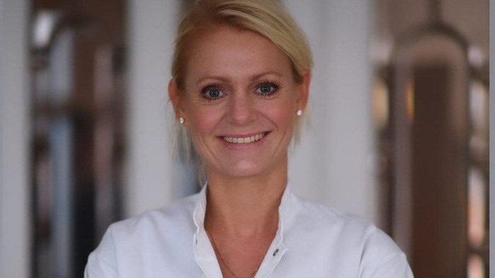 En kvinde med blond hår og et smil, der bør i en hvid bluse.