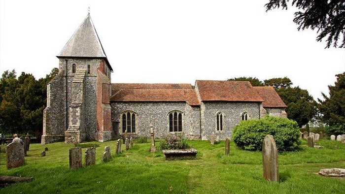 Church with stone tower and red roof, surrounded by gravestones in a green cemetery.