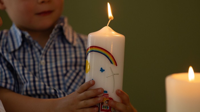 Ein Junge hält eine bunte Kerze in der Hand, während eine weitere Kerze im Hintergrund brennt