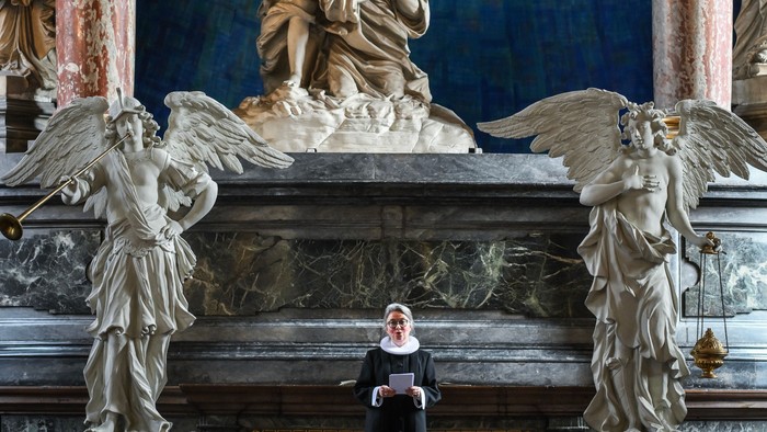 En præst står i en prægtig kirke med store skulpturer og billeder af engle.