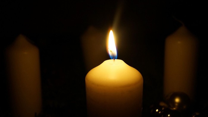 Tre stearinlys, ét tændt, i mørket