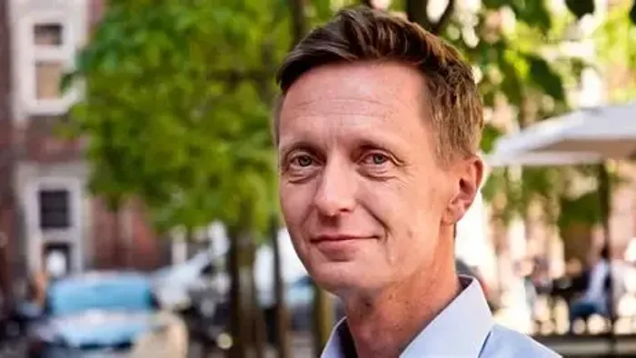 En mand står på en gade med træer og bygninger i baggrunden.