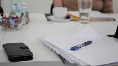 En skrivebord med notebog, pen, mobiltelefon og en kop kaffe.