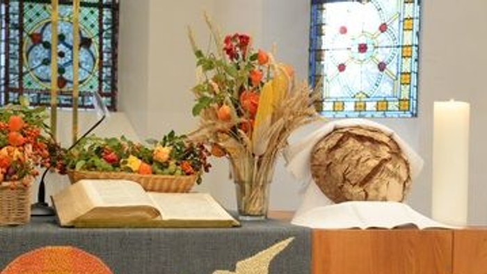 Ein Tisch in einer Kirche mit Blumen, Kerzen und Brot vor einem Fenster mit buntem Glas