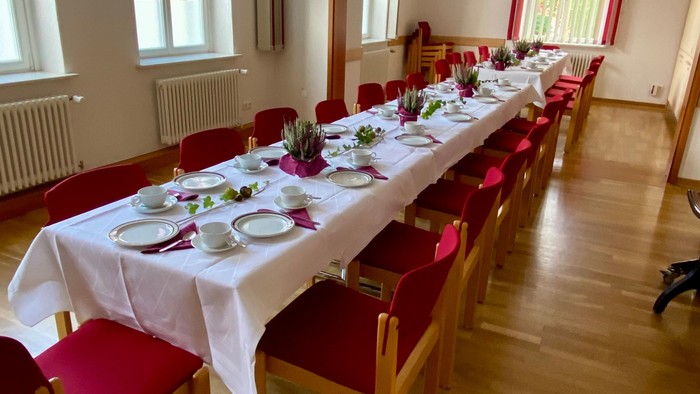 Ein langer Tisch mit weißer Tischdecke und roten Stühlen, fein gedeckt für ein Essen