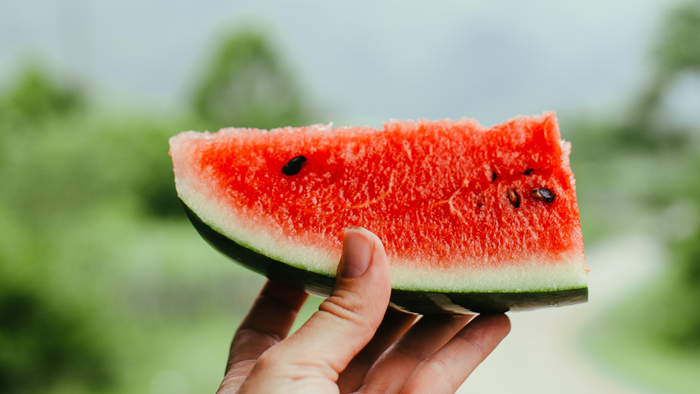 Eine Hand hält ein Stück Wassermelke mit roter Fruchtfleisch und schwarzen Samen.