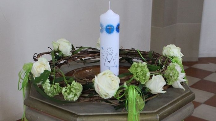 Ein kleiner Tisch mit weißer Kerze und grünen Blumen.